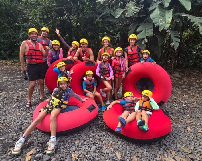 A group of people wearing helmets and life vests sitting on red inflatable tubes outdoors. 3