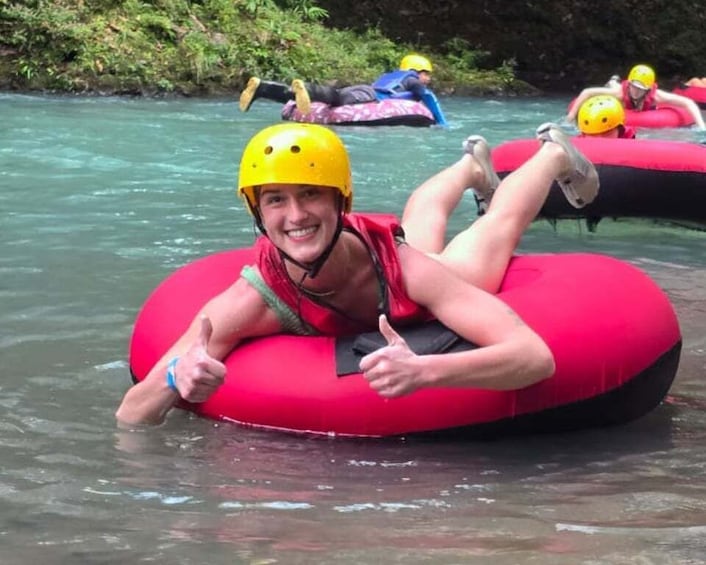 A person on a red inflatable raft in a river with other rafts and people in the background. 1