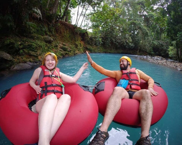 Two people in red inflatable tubes on a river surrounded by greenery. 2