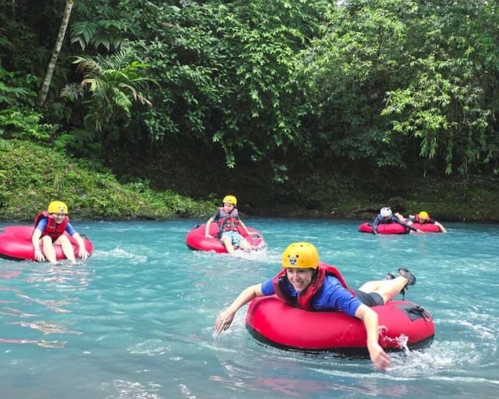 People floating on red inner tubes in a river surrounded by dense greenery. 4