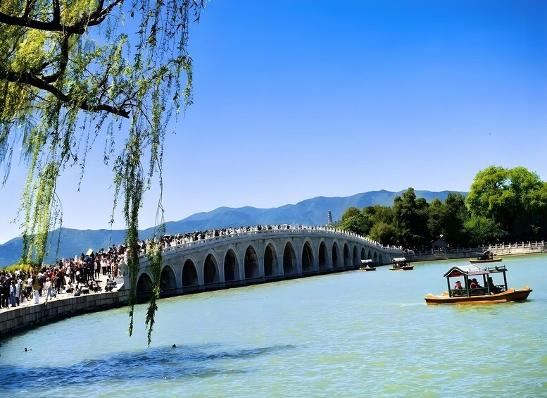 A stone bridge over a calm river with people on it and a boat in the water. 2