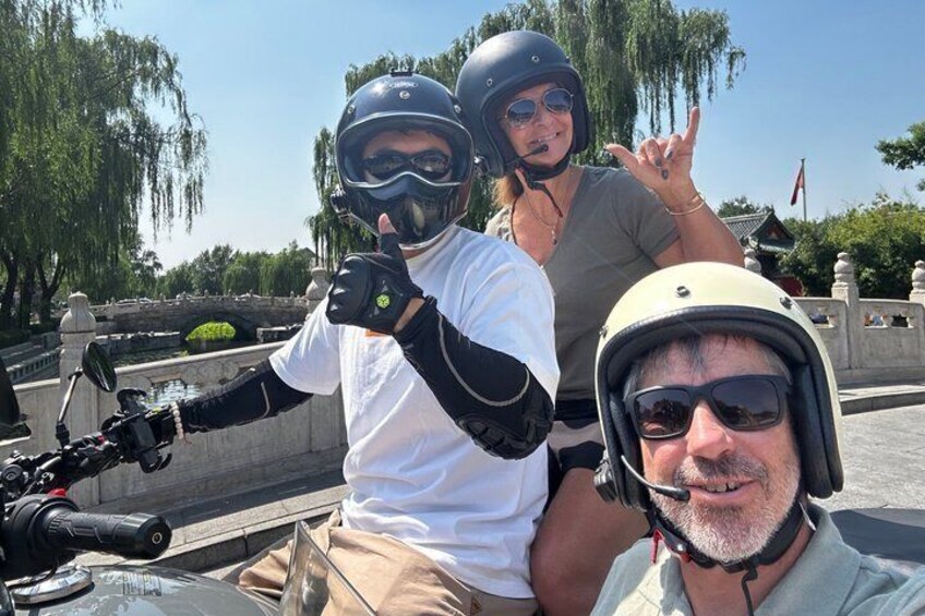 Een persoon op een motor met een helm, een andere persoon achterop en een derde persoon op de voorgrond. 4