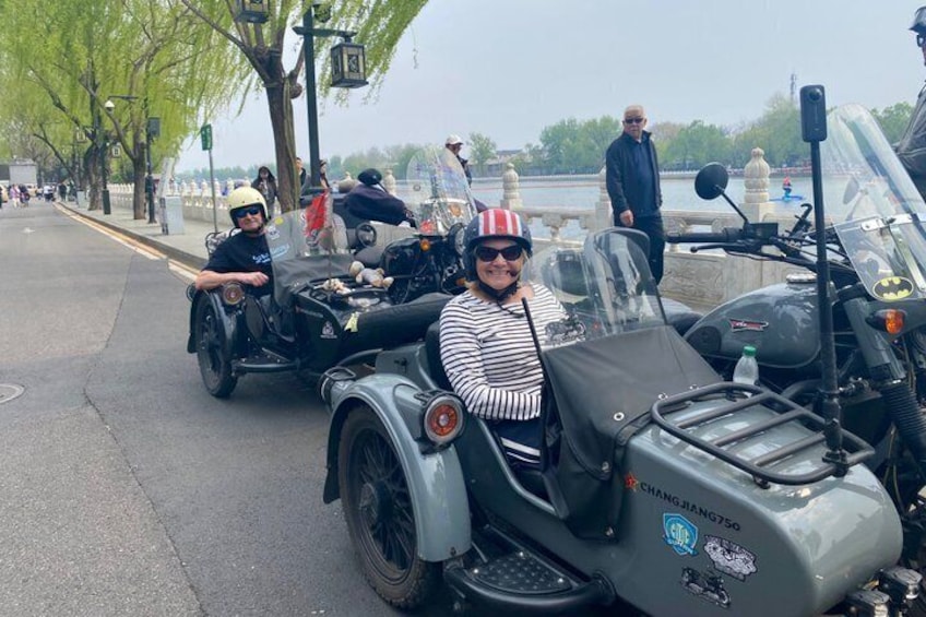Een klassieke motor met zijspan, een persoon in een gestreepte shirt en een rood-witte hoed, en een persoon in een zwart shirt en helm. 3