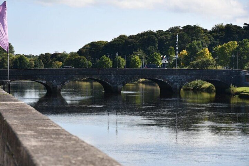 A stone bridge over a calm river with a flag on the left and trees in the background. 5