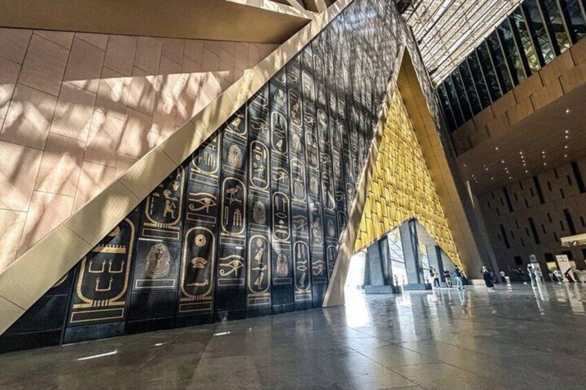 A modern building with a large wall of ancient Egyptian hieroglyphs and a geometric yellow structure. 4