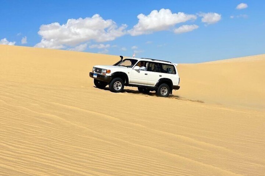 A white SUV driving through a desert with sand dunes. 4