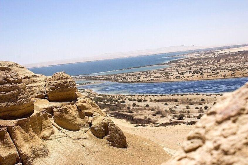 A desert landscape with rocky outcrops and a distant view of a coastline. 3