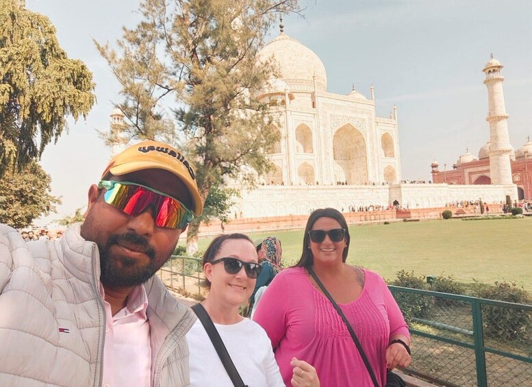 Three people taking a photo with the Taj Mahal in the background. 1