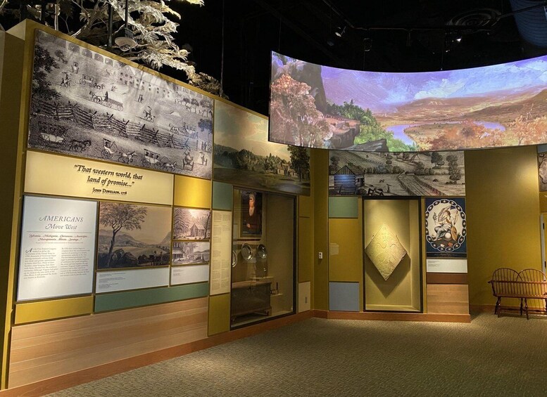 A museum exhibit with historical photographs, a quote plaque, and a large projection screen. 2