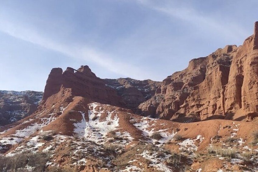 A desert landscape with red rock formations and patches of snow. 3
