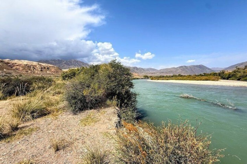 A river with clear water, surrounded by dry shrubs and mountains in the background. 2