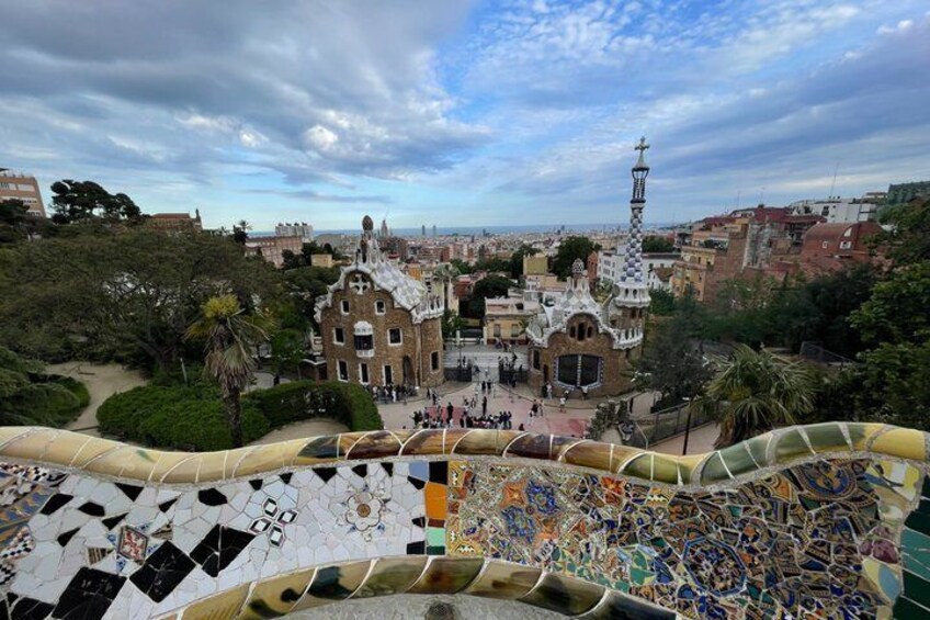 A view of a park with a mosaic floor, a building with a tower, and a cityscape in the background. 2