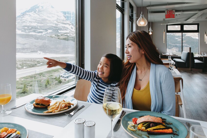 A dining table with food and a glass of wine, a mountain view through a window, and a sign indicating an exit. 3