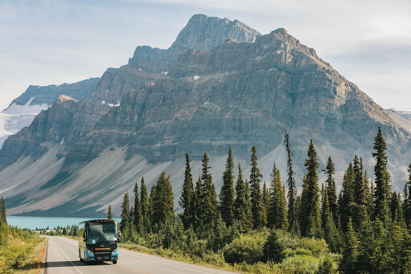 A bus on a road with a mountain and a lake in the background. 2