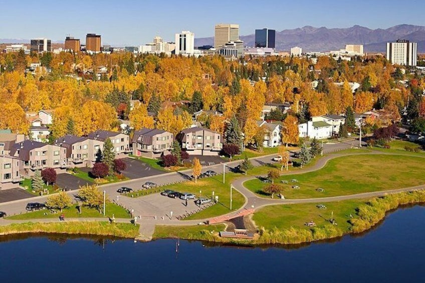 Un quartier résidentiel au bord d’un lac, avec des arbres aux couleurs automnales, une petite île et, au loin, la silhouette d’une ville. 5
