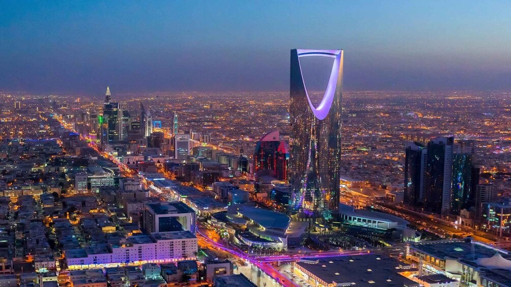 A cityscape at dusk with a prominent modern skyscraper featuring a unique, illuminated design. 1