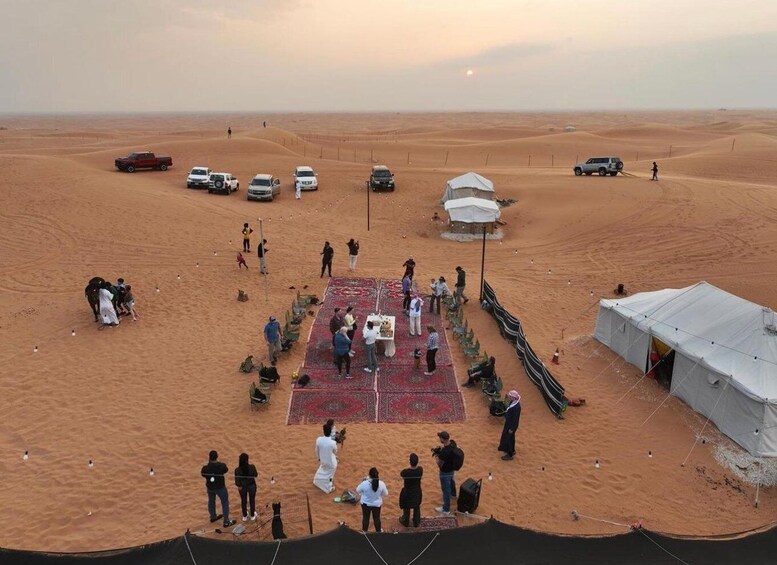 A desert with tents and people gathered around a central area with a red carpet. 3