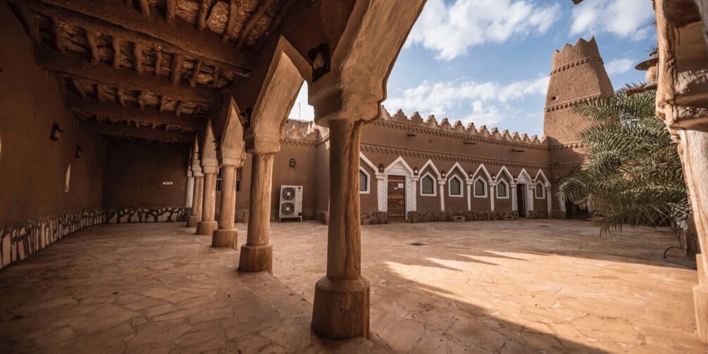 An architectural courtyard with arches, a tower, and a palm tree. 2