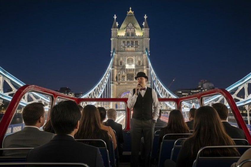 A person speaking to an audience on a red double-decker bus with the Tower Bridge in the background. 4