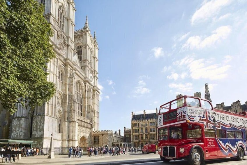 A red double-decker bus with 'The Classic Tour' written on it, driving past a historic cathedral. 1