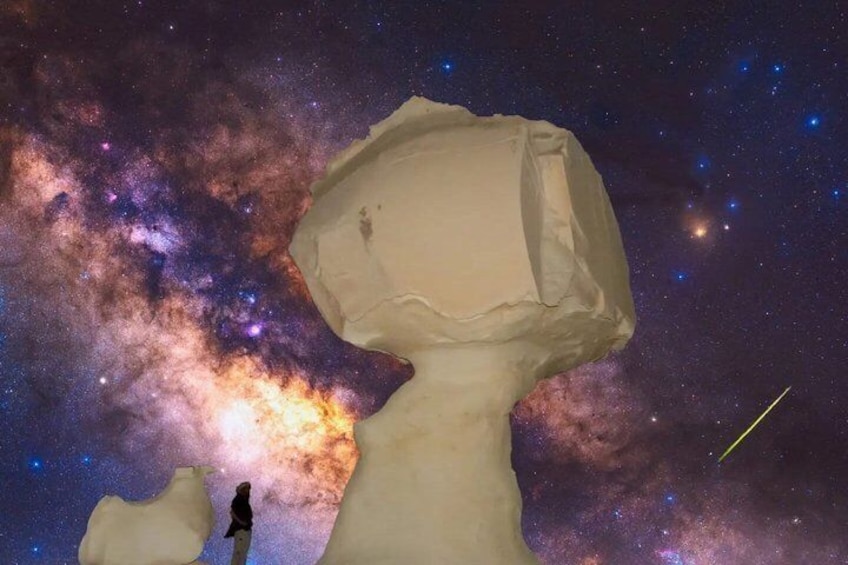 Une grande formation rocheuse, avec une personne debout à côté, se dressant sur fond de ciel étoilé. 1