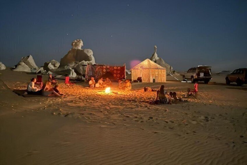 Un campement dans le désert, avec des tentes et un feu de camp, entouré de grandes formations rocheuses. 2