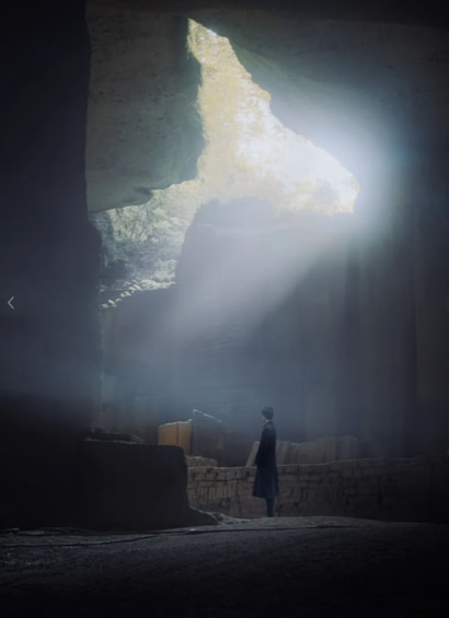 A person standing in a dimly lit cave with a large rock formation above them. 5