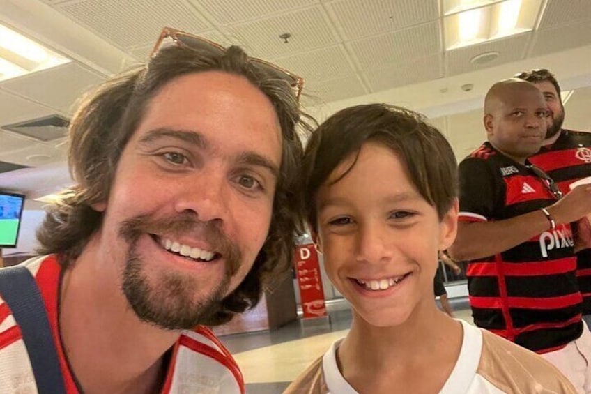 Un hombre y un niño en un aeropuerto, con una camiseta deportiva al fondo. 2