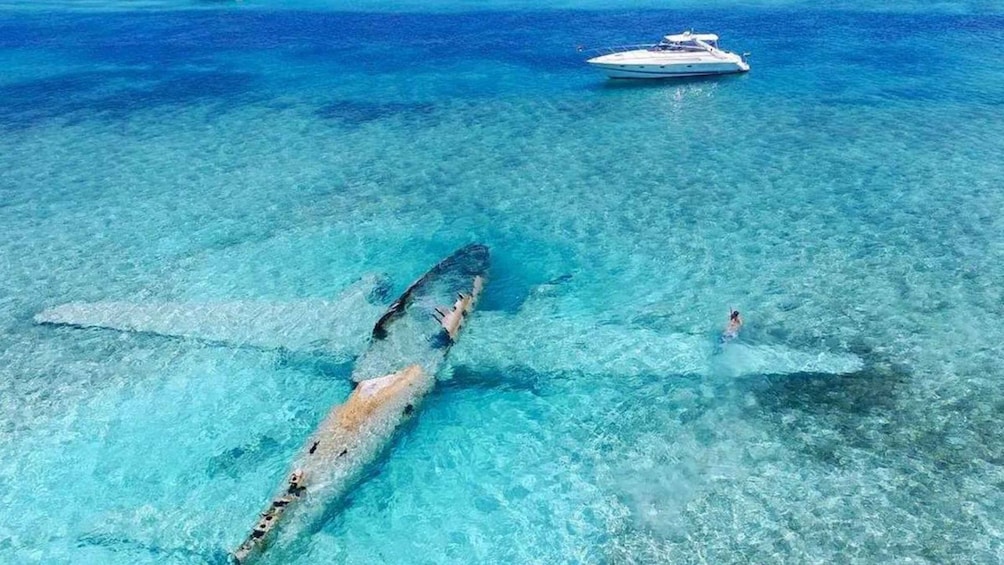 A sunken shipwreck in clear turquoise waters with a yacht in the background. 5