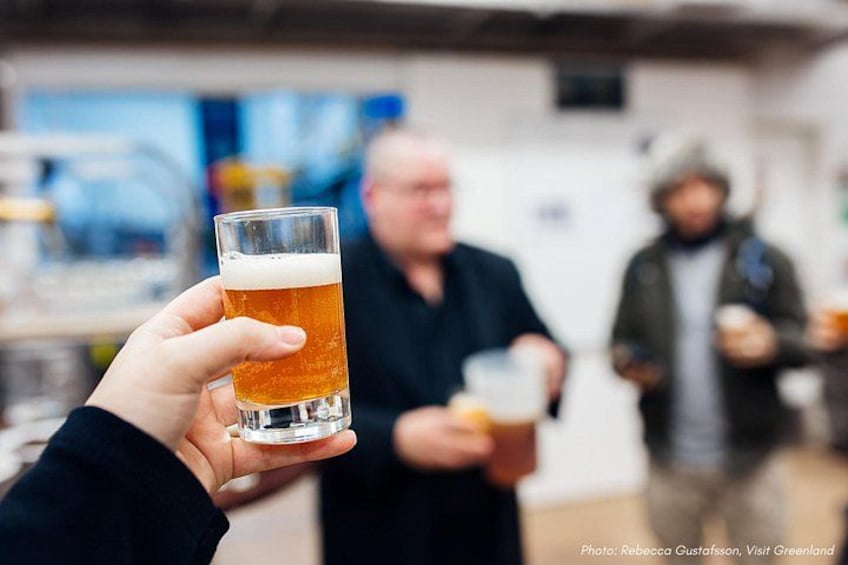 A person holding a glass of beer, with a blurred background of a bar or pub setting. 5