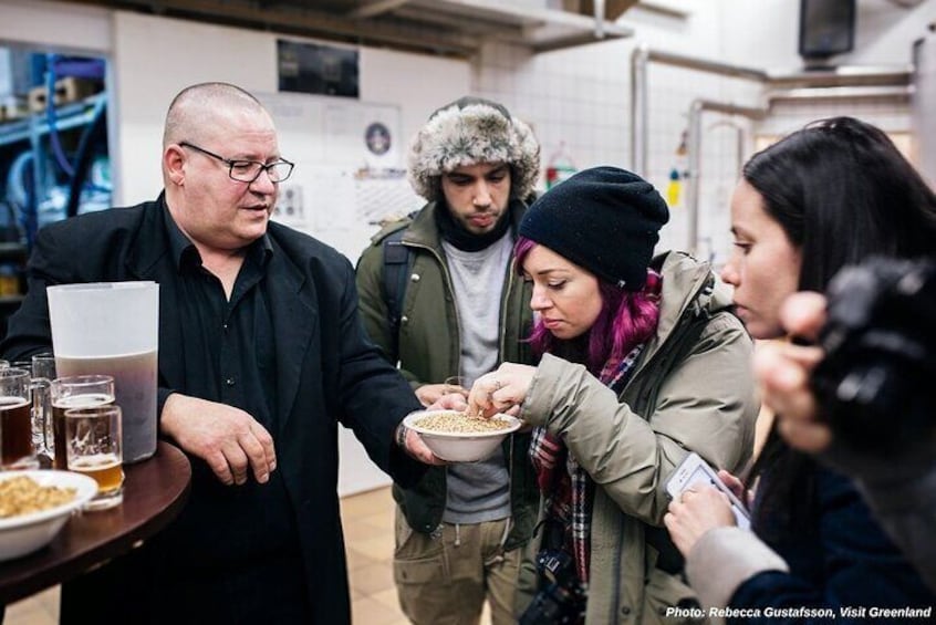 A group of people gathered around a table with food and drinks, in an indoor setting with shelves and equipment in the background. 2