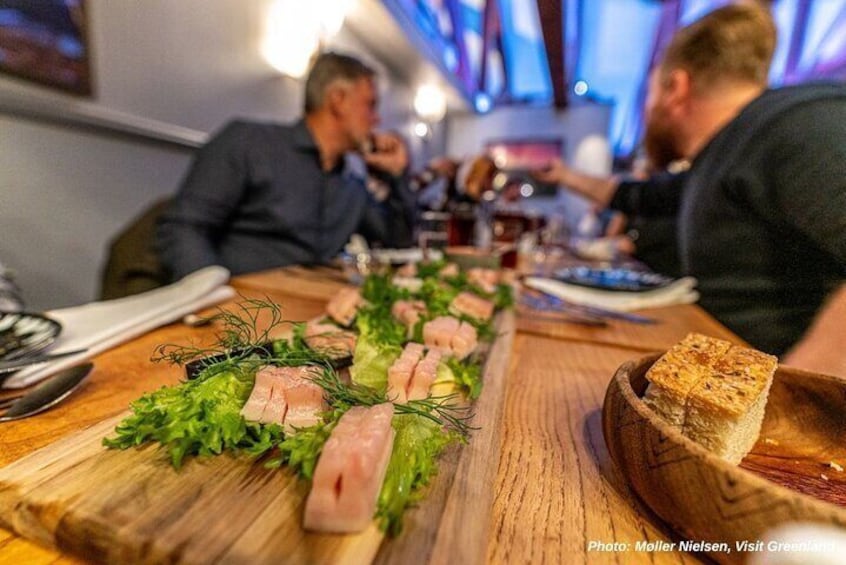 A wooden serving board with sliced meat, greens, and bread. 3
