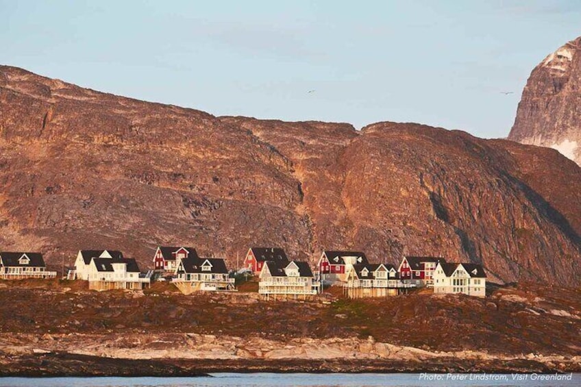 A row of traditional houses with red roofs and white walls, situated on a hillside with a rocky backdrop. 5