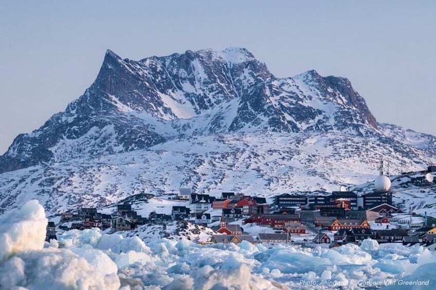 A snow-covered town with buildings and mountains in the background. 1