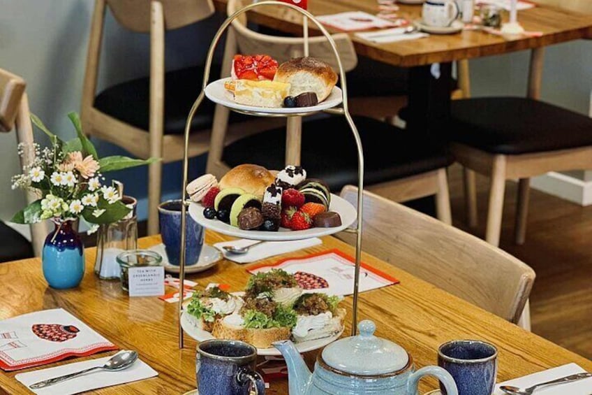 A wooden table with a tiered dessert stand, a vase with flowers, and a teapot. 4