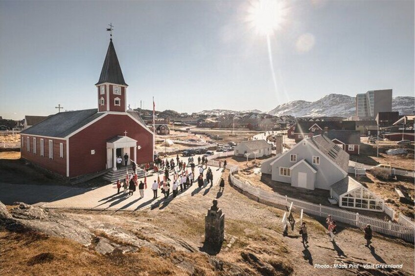 A red church with a steeple, a white building, and a mountainous backdrop. 1