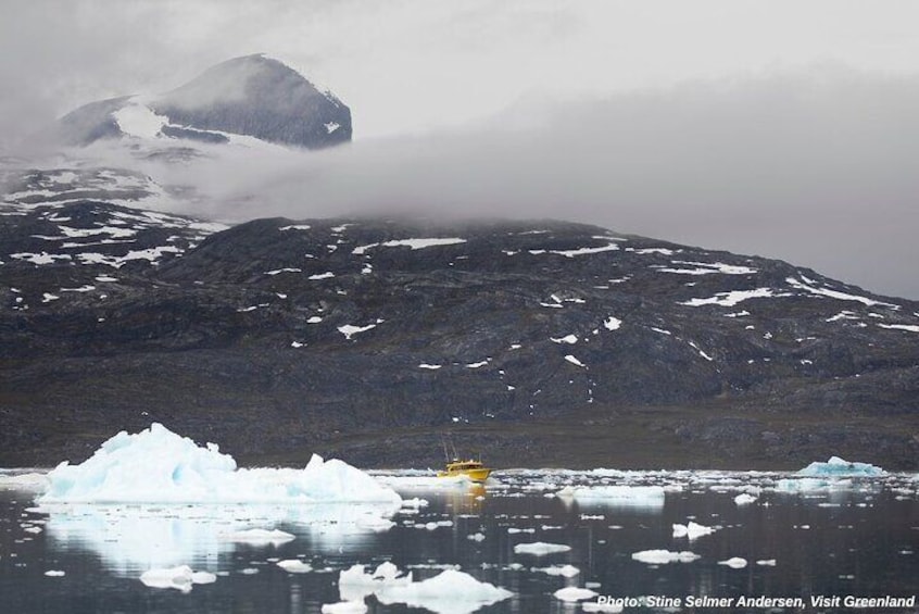 A glacier with icebergs, a mountain, and a yellow boat. 2