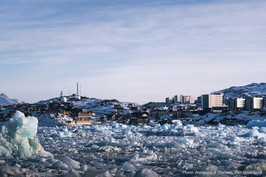 A snowy landscape with buildings and a large iceberg in the foreground. 1