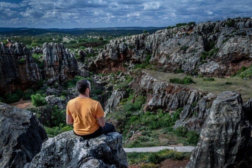 Une personne assise sur un rocher, d’où elle contemple un paysage accidenté, avec des falaises et une végétation clairsemée. 3