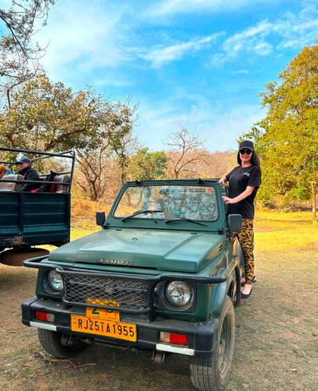 A green Maruti car with a license plate in a rural setting with trees and clear skies. 2