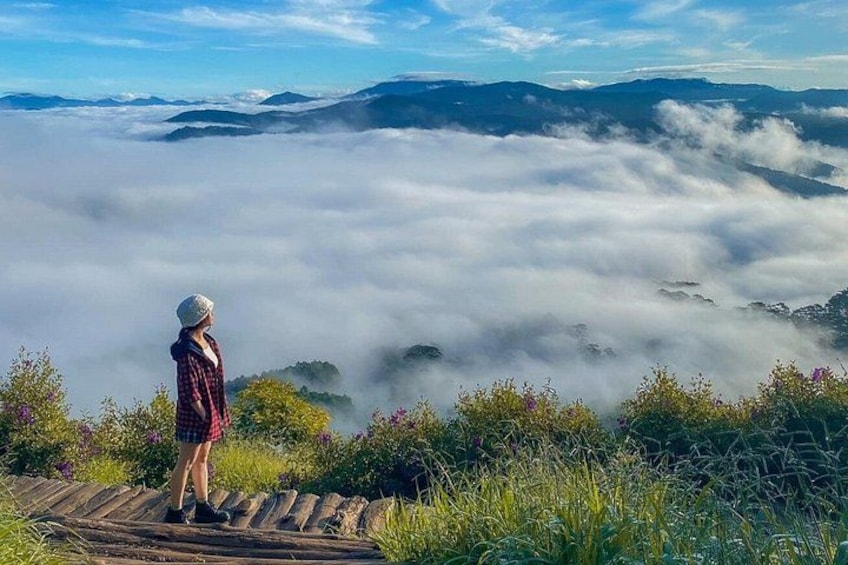 A person standing on a wooden platform overlooking a valley with clouds below. 2