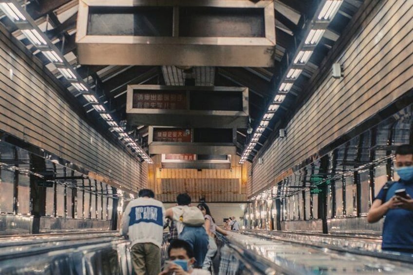 Een metrostation met roltrappen, borden bovenin en reizigers. 2