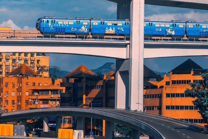 Een blauwe trein op een verhoogd spoor boven een stadsgezicht met gebouwen en een brug. 1