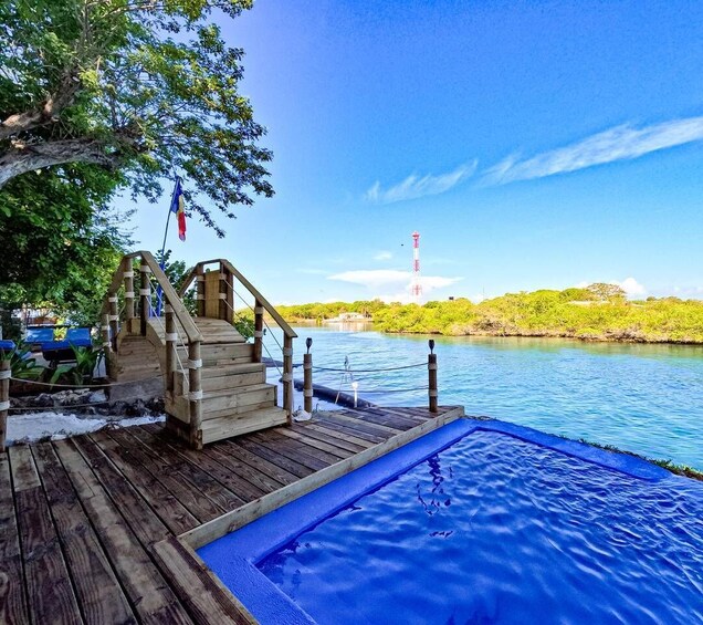 A wooden deck with a small staircase leading to a pool, surrounded by water and greenery. 2