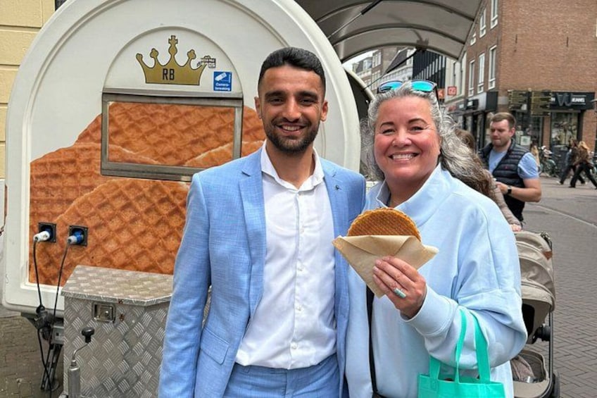 Een persoon in een lichtblauwe pak staat naast een foodtruck met een display van wafels. 1