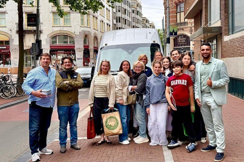Een groep mensen staat op een stoep met een gebouw en een bus op de achtergrond. 4