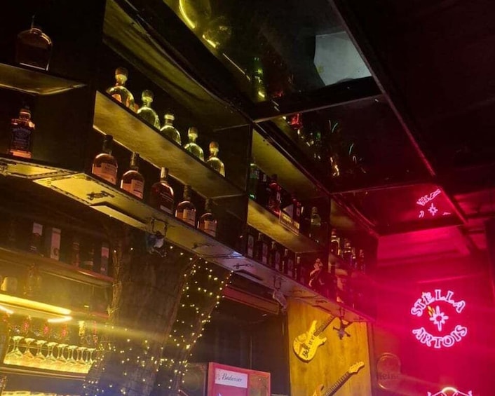 A bar with shelves of liquor bottles, a guitar, and a neon sign. 3