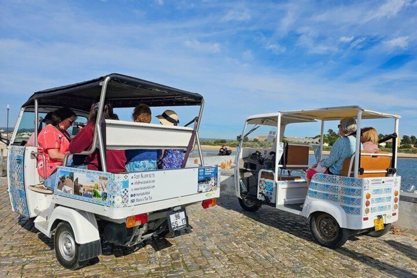 Two open-top vehicles parked on a cobblestone waterfront. 1