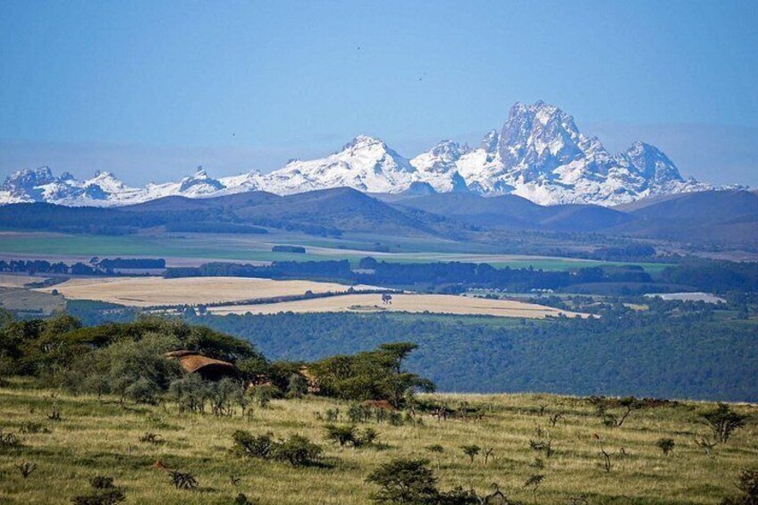 A mountainous landscape with snow-capped peaks, a grassy field, and a small bridge. 2