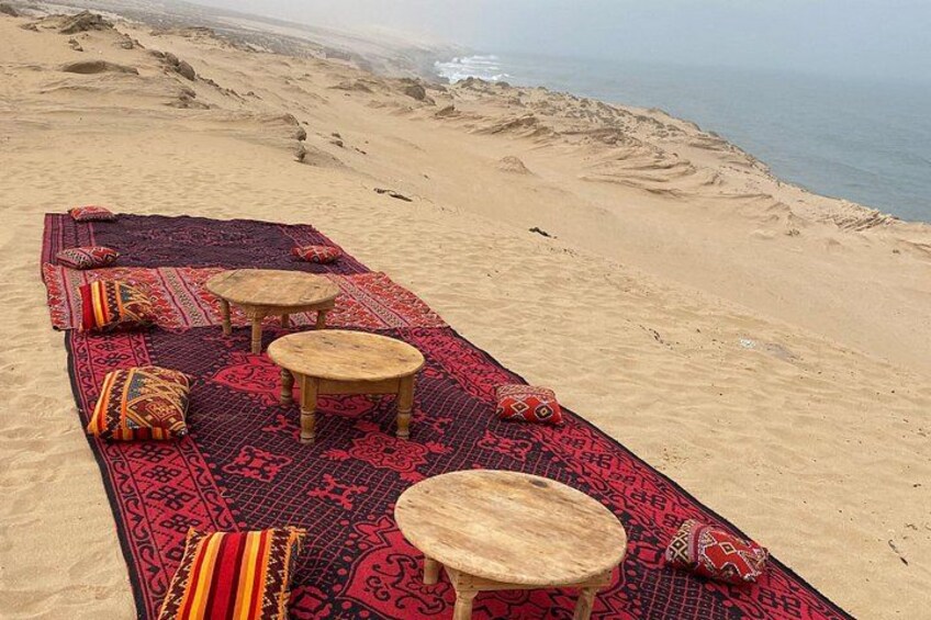 A beach with a red patterned mat and wooden stools. 3